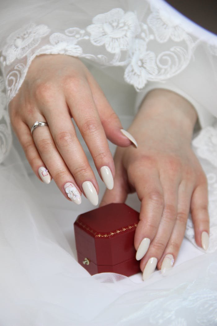 Close-up of a bride's hands showcasing elegant nails and a wedding ring.